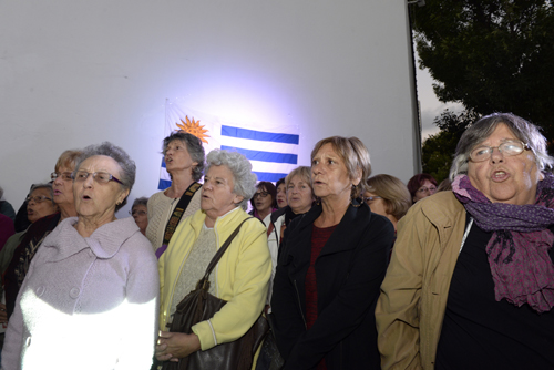 Mujeres entonando el himno con la bandera nacional al costado