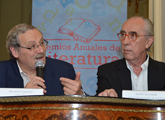 Se ve al ministro de Cultura y al director Nacional de cultura sentados hablando con el logo de los Premios Anuales de Literatura detrás